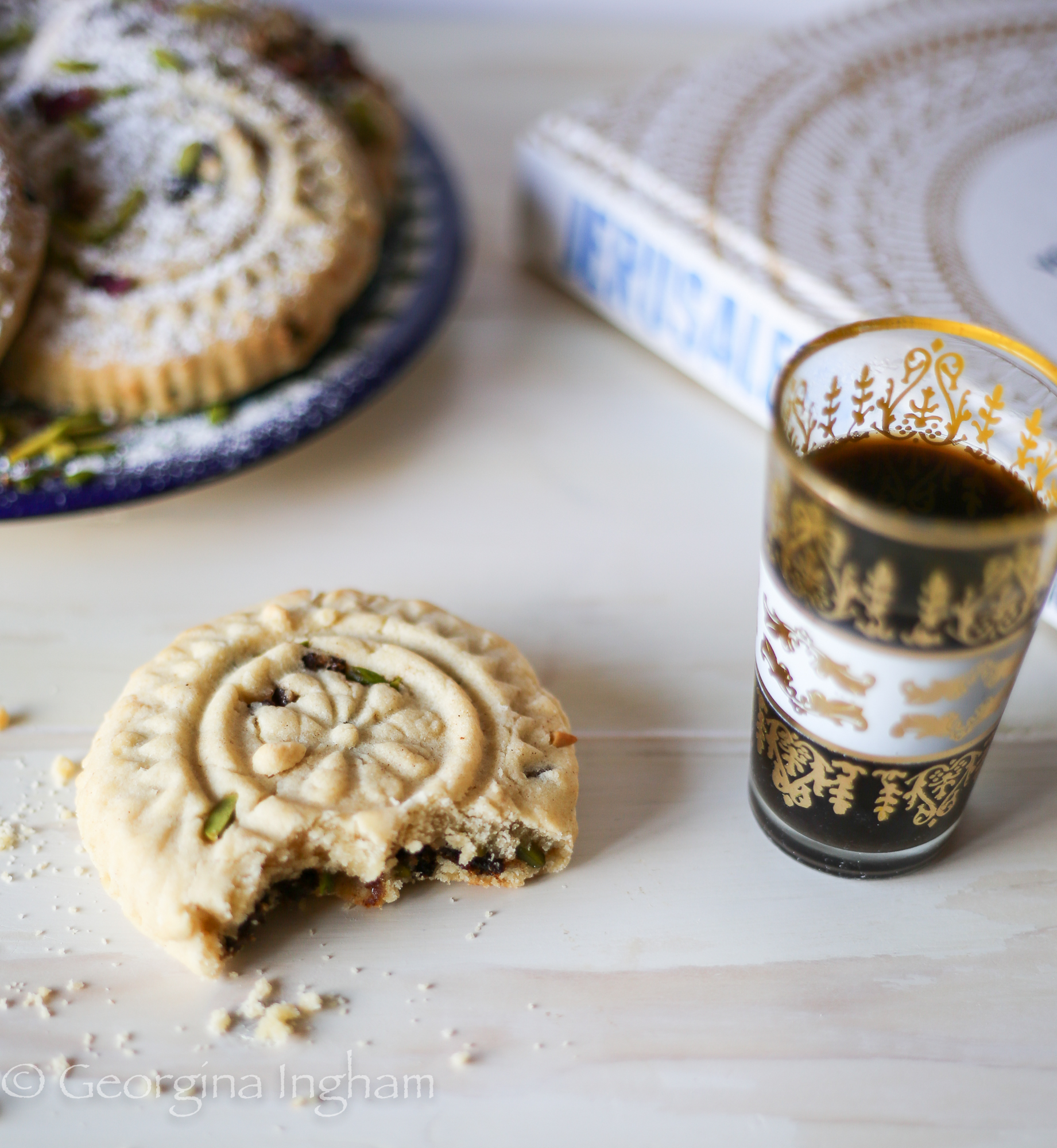 Bitten ma&rsquo;amoul cookie showing date and pistachio filling beside a small cup of Arabic coffee